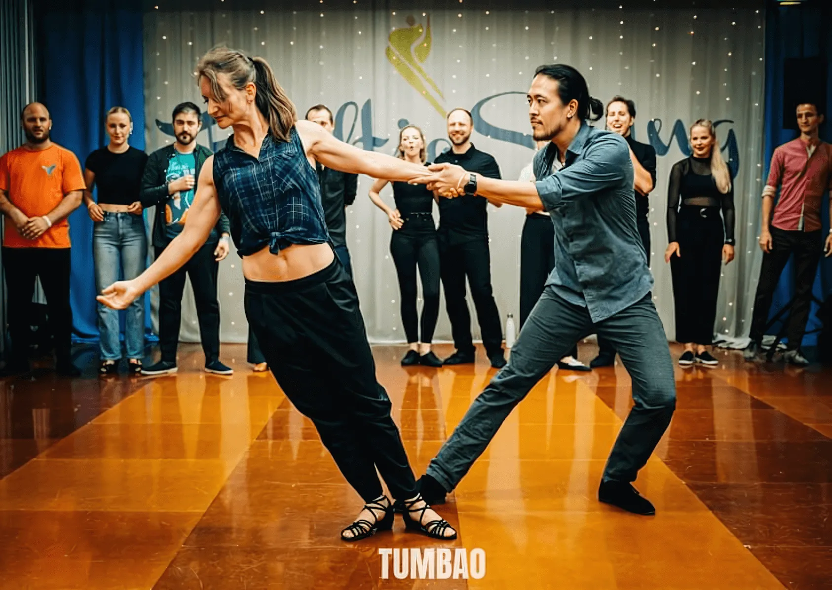 Tschen Fung Wang and Evgenia Itkina performing an athletic West Coast Swing move with spectators watching. Image by Eric Tumbao Pix.