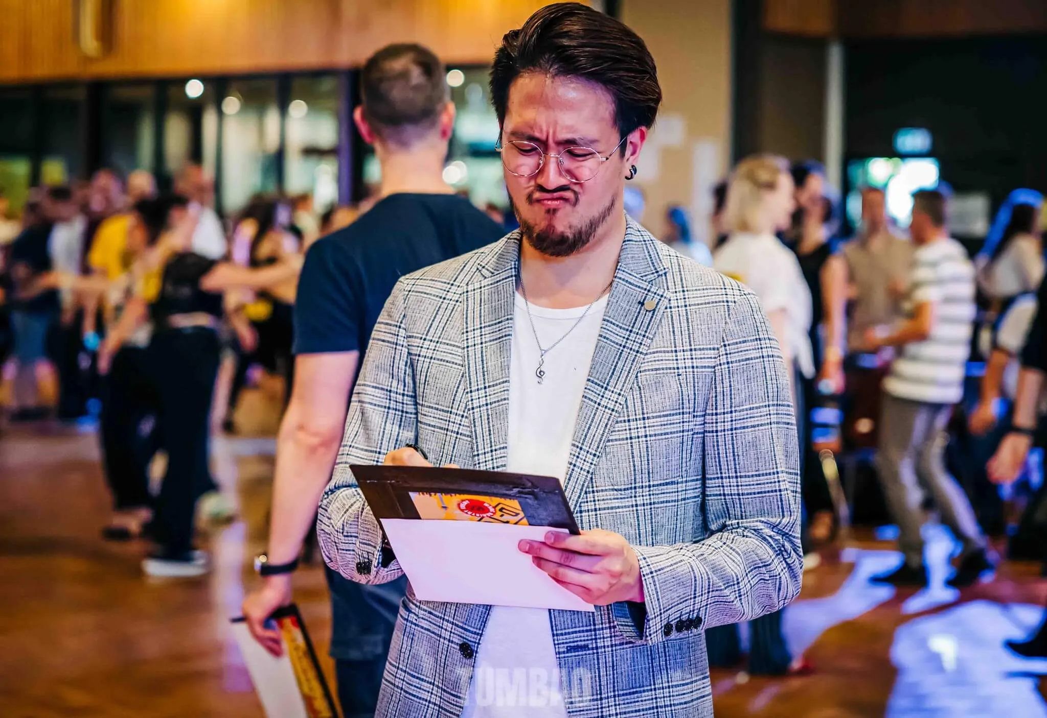 Tschen Fung Wang judging West Coast Swing competition, wearing checked blazer while reviewing scoring sheets at dance event. Image by Eric Tumbao Pix.